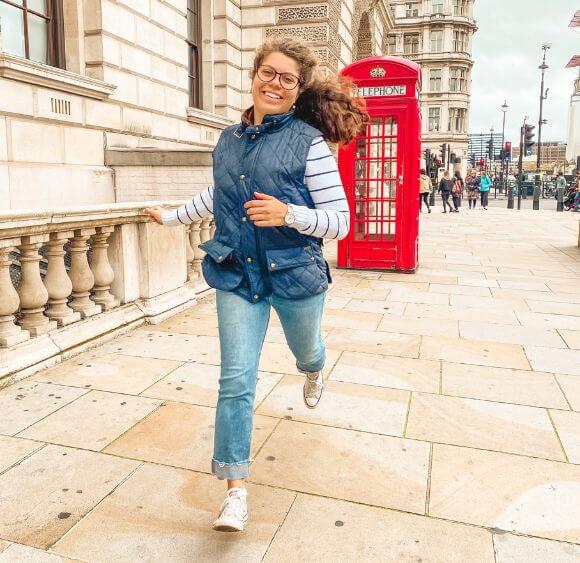 Miriam owner of MiriamMemoirs, running through the white limestone buildings of Westminster in London with a red telephone machine behind her.
