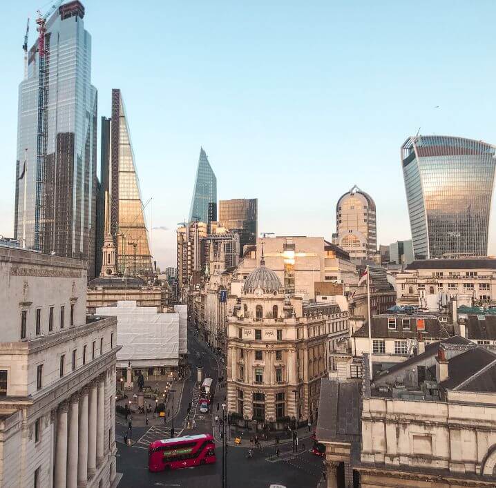 The city of London during sunset with a red bus passing
